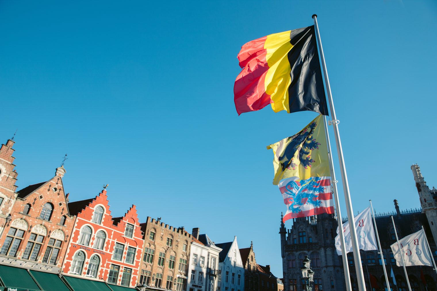 Un drapeau belge flotte fièrement sous un ciel bleu dégagé, ses trois bandes verticales noire, jaune et rouge vives captant immédiatement l&amp;apos;attention.